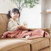 Little girl reading a book sitting with a pink receiving blanket.