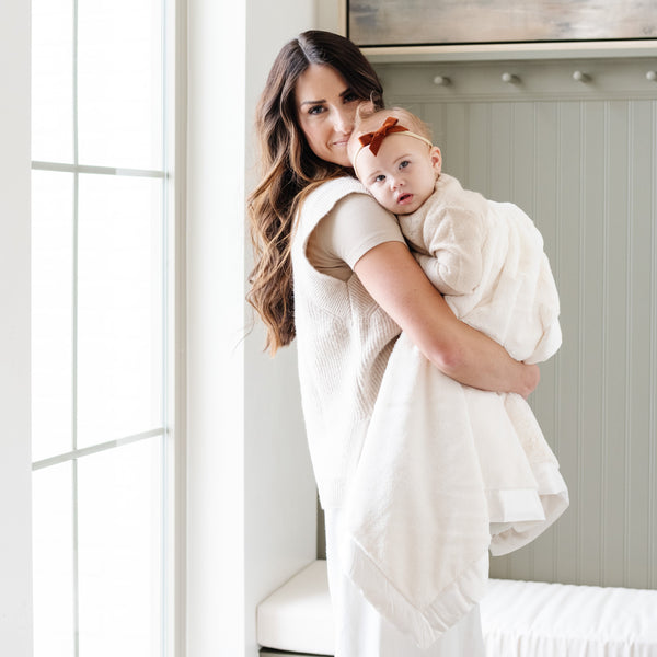 Mother holding baby girl wrapped in luxurious ivory receiving blanket.