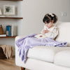 Little girl reading book on couch with a light purple receiving blanket.