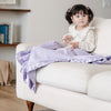 Little girl reading book and playing on couch with a light purple receiving blanket.