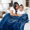 A mother and her son sit under a Luxury Extra Large Oversized Throw Navy Colored Lush Saranoni Blanket. The soft blanket is an extra large throw blanket and has a soft faux fur feeling.