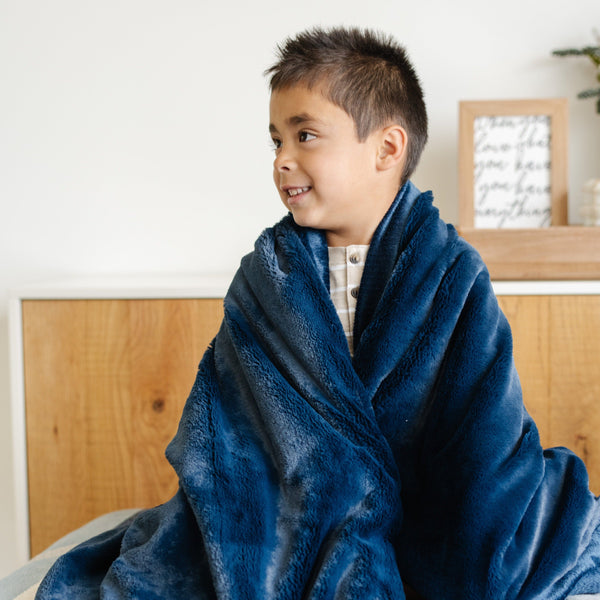 A little boy is wrapped in a Toddler Navy Colored Lush Luxury Saranoni Blanket. The soft blanket is small blanket and a baby blanket or toddler blanket.