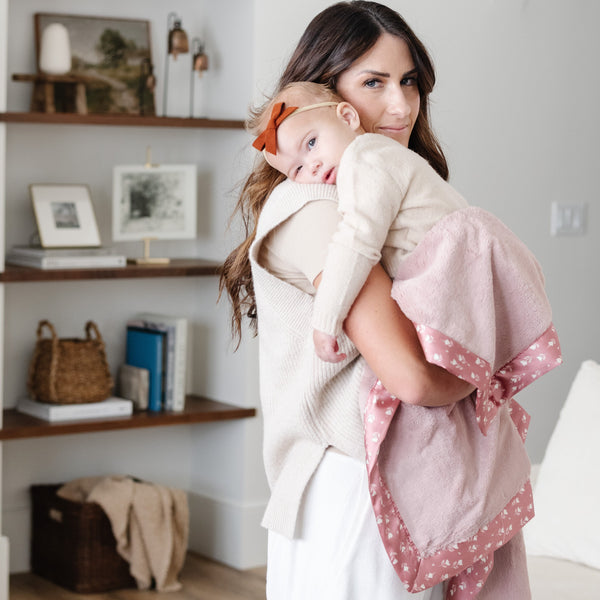 Mother holding baby girl wrapped in a soft pink receiving blanket. 