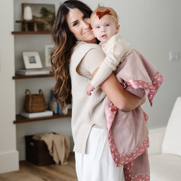 Mother and daughter snuggling together wrapped in a cozy, pink receiving blanket.