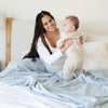 A mother holds her son while sitting under a Luxury Extra Large Oversized Throw Chambray (cloud-like light blue) Colored Lush Saranoni Blanket. The soft blanket is an extra large throw blanket and has a soft faux fur feeling.