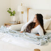 A woman lays on a Luxury Extra Large Oversized Throw Chambray (cloud-like light blue) Colored Lush Saranoni Blanket. The soft blanket is an extra large throw blanket and has a soft faux fur feeling.