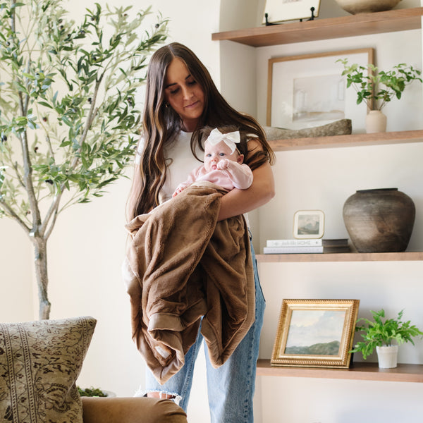 A mother holds her baby girl and a Luxury Receiving Hazelnut Colored Lush Saranoni Blanket. The soft blanket is a small blanket and a baby blanket or toddler blanket.