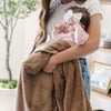 A mother holds her baby girl and a Luxury Receiving Hazelnut Colored Lush Saranoni Blanket. The soft blanket is a small blanket and a baby blanket or toddler blanket.