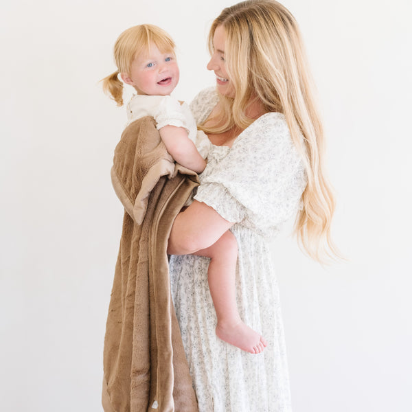 A mother holds her daughter and a Toddler Hazelnut Colored Lush Luxury Saranoni Blanket. The soft blanket is a baby blanket or toddler blanket.