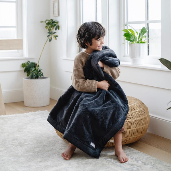 A little boy hugs a Luxury Receiving Charcoal Colored Lush Saranoni Blanket. The soft blanket is a small blanket and a baby blanket or toddler blanket.