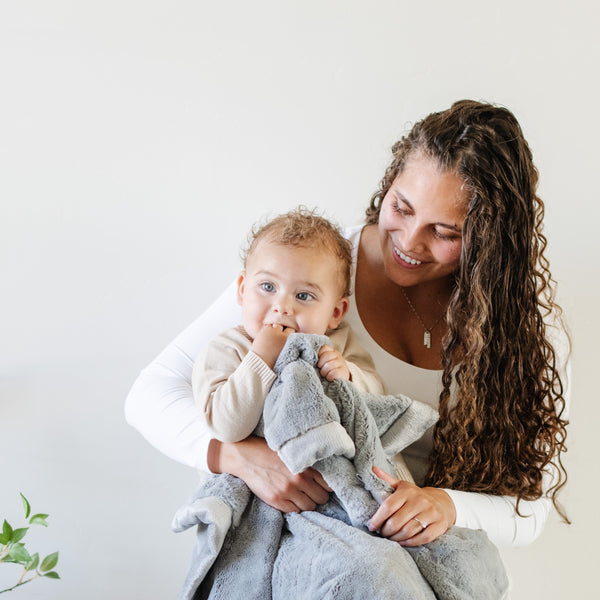 A mother holds her baby boy who has a Gray Colored Lush Saranoni Blanket draped over him. The soft blanket is a small blanket and a baby blanket or toddler blanket.