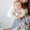 A mother holds her baby boy and a Luxury Receiving Gray Colored Lush Saranoni Blanket over her baby boy's lap. The soft blanket is a small blanket and a baby blanket or toddler blanket.