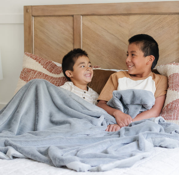 Two little boys who are brothers sit under a Luxury Toddler Gray Colored Lush Saranoni Blanket. The soft blanket is a toddler blanket or baby blanket.