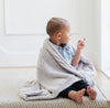 A little boy wrapped in a Luxury Receiving Feather (light gray) Colored Lush Saranoni Blanket. The soft blanket is a small blanket and a baby blanket or toddler blanket.