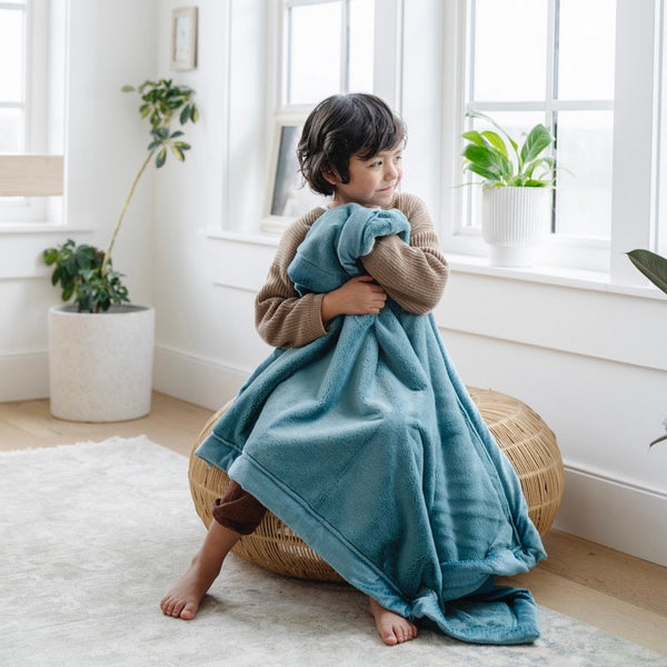 A little boy holds a Luxury Receiving Mineral Blue Colored Lush Saranoni Blanket. The soft blanket is a small blanket and a baby blanket or toddler blanket.