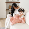 A mother and her little girl sit under a Luxury Receiving Blossom (light peachy pink) Colored Lush Saranoni Blanket. The soft blanket is a small blanket and a baby blanket or toddler blanket.