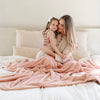 A mother and her daughter sit under a Luxury Extra Large Oversized Throw Blossom (light peachy pink) Colored Lush Saranoni Blanket. The soft blanket is an extra large throw blanket and has a soft faux fur feeling.