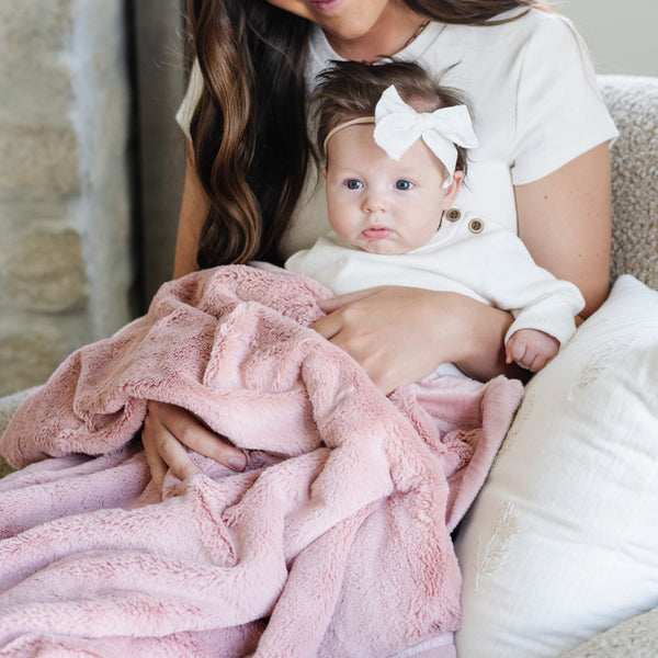 A mother holds her baby girl in a Luxury Receiving Ballet Slipper (light pink) Colored Lush Saranoni Blanket. The soft blanket is a small blanket and a baby blanket or toddler blanket.