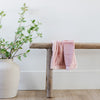 A Mini Saranoni Lush Blanket that is light pink is draped over a wood bench. 