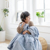 A little boy sits under a Luxury Receiving Storm Cloud (dusty blue gray) Colored Lush Saranoni Blanket. The soft blanket is a small blanket and a baby blanket or toddler blanket.