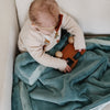 A little girl sits under a Luxury Receiving Eucalyptus Colored Lush Saranoni Blanket. The soft blanket is a small blanket and a baby blanket or toddler blanket.