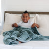 A little boy sits under a Luxury Toddler Eucalyptus Colored Lush Saranoni Blanket. The soft blanket is a toddler blanket or baby blanket.