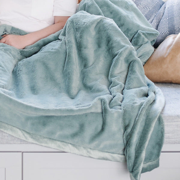 A Luxury Extra Large Oversized Throw Eucalyptus Colored Lush Saranoni Blanket. The soft blanket is an extra large throw blanket and has a soft faux fur feeling.