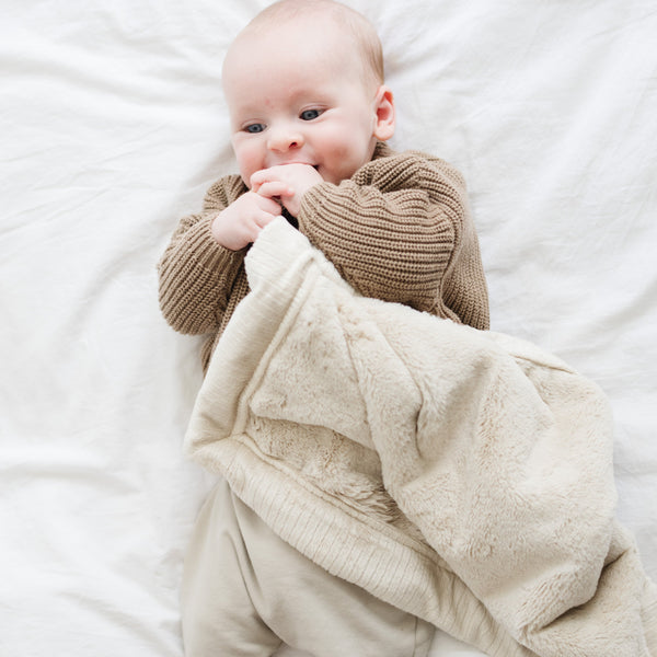 A baby boy holds a Mini Buttermilk (light tan) Colored Lush Saranoni Blanket. The soft blanket is a small blanket and a baby blanket or toddler blanket.