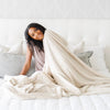 A woman holds a Luxury Extra Large Oversized Throw Buttermilk (light tan) Colored Lush Saranoni Blanket. The soft blanket is an extra large throw blanket and has a soft faux fur feeling.