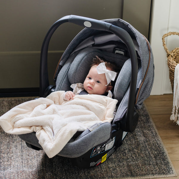 A baby girl lays in her carseat with a Natural (off-white) Colored Lush Saranoni Blanket draped over her. The soft blanket is a small blanket and a baby blanket or toddler blanket.