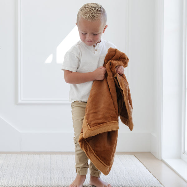 A little boy carries a Luxury Receiving Camel (light yellowish brown) Colored Lush Saranoni Blanket. The soft blanket is a small blanket and a baby blanket or toddler blanket.