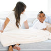 A mother and son sit under a Luxury Extra Large Oversized Throw Natural (off-white) Colored Lush Saranoni Blanket. The soft blanket is an extra large throw blanket and has a soft faux fur feeling.