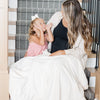 A mother and daughter sit under a Luxury Extra Large Oversized Throw Natural (off-white) Colored Lush Saranoni Blanket. The soft blanket is an extra large throw blanket and has a soft faux fur feeling.