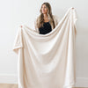 A woman holds a Luxury Extra Large Oversized Throw Natural (off-white) Colored Lush Saranoni Blanket. The soft blanket is an extra large throw blanket and has a soft faux fur feeling.