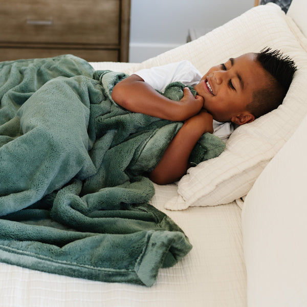 A little boy holds a Toddler Hunter Green Colored Lush Luxury Saranoni Blanket. The soft blanket is small blanket and a baby blanket or toddler blanket.