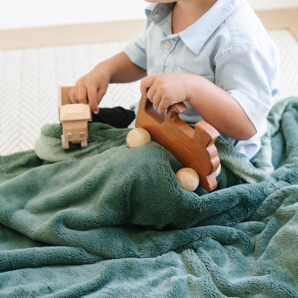 A little boy sits under a Luxury Receiving Hunter Green Colored Lush Saranoni Blanket while playing with toys. The soft blanket is a small blanket and a baby blanket or toddler blanket.