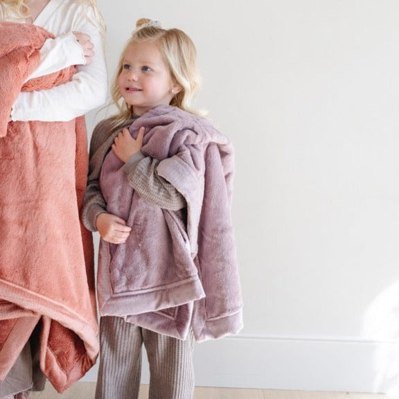 A little girl holds a Luxury Receiving Bloom (dusty purple) Colored Lush Saranoni Blanket. The soft blanket is a small blanket and a baby blanket or toddler blanket.