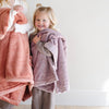 A little girl holds a Luxury Receiving Bloom (dusty purple) Colored Lush Saranoni Blanket. The soft blanket is a small blanket and a baby blanket or toddler blanket.