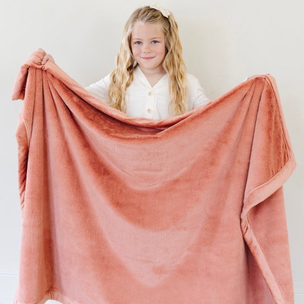 A little girl holds up a Luxury Toddler Clay Colored Lush Saranoni Blanket. The soft blanket is a toddler blanket or baby blanket.