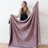 A woman holds a Luxury Extra Large Oversized Throw Bloom (dusty purple) Colored Lush Saranoni Blanket. The soft blanket is an extra large throw blanket and has a soft faux fur feeling.