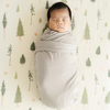 Baby boy swaddled in Saranoni stretchy swaddle while laying on Pine Cotton Muslin Crib Sheet.