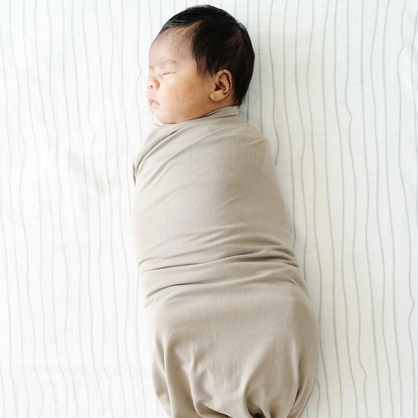 Baby boy swaddled and laying on Breezy Stripe Cotton Muslin Crib Sheet. 