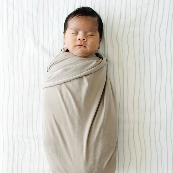 Baby boy laying on Breezy Stripe Cotton Muslin crib sheet. 