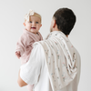 Baby in a pink outfit with a bow, held by dad holding a floral-patterned blanket.