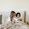 A mother sits reading a book with her son. They have a khaki patterned faux fur blanket on their lap. The soft blanket is a Saranoni blanket and a luxury blanket. 