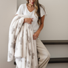 Woman holds a cream and tan swiss cross double layer bamboni xl blanket. 