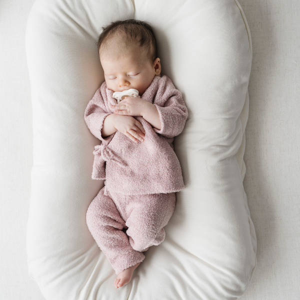 Newborn baby in a pink outfit lying on a white cushion