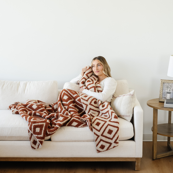 Woman snuggled on couch with Khmer Double Layer Bamboni Throw soft blanket.