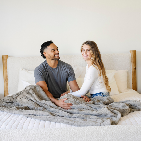 A husband and wife sit with a grayish brown patterned faux fur blanket on their laps. The soft blanket is a Saranoni blanket and a luxury blanket. 