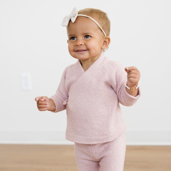 Baby in pink outfit with a white bow headband on a plain background